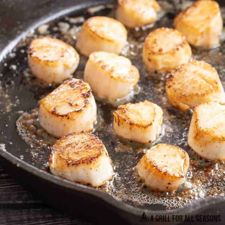 scallops being cooked in butter in a cast iron skillet