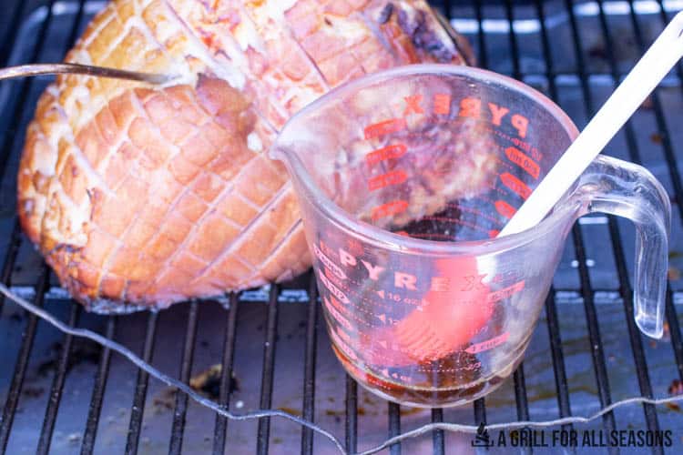 Ham on smoker with glaze in measuring cup