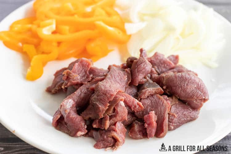 raw venison strips on a white plate with uncooked onion and pepper slices