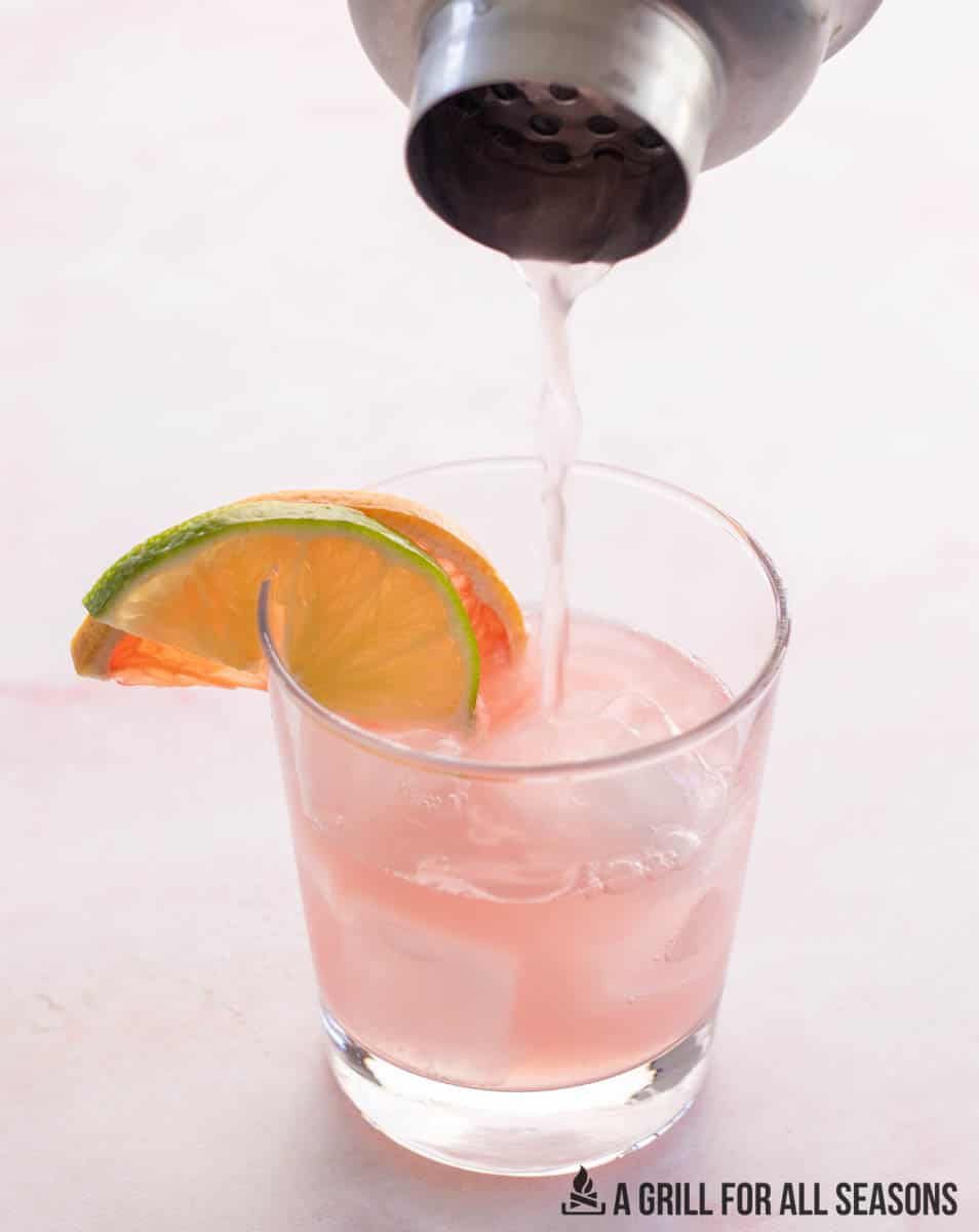 pink paloma being poured from cocktail mixer into glass