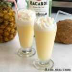 two tall glass of bacardi pina colada with whipped cream and straws