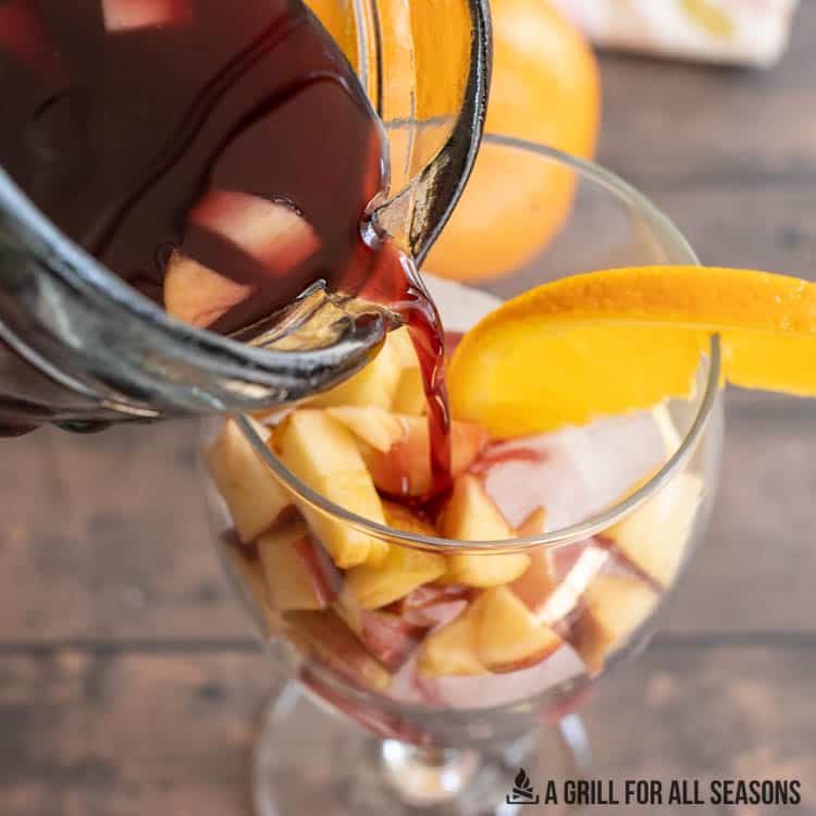 sangria being poured from pitcher into glass of ice