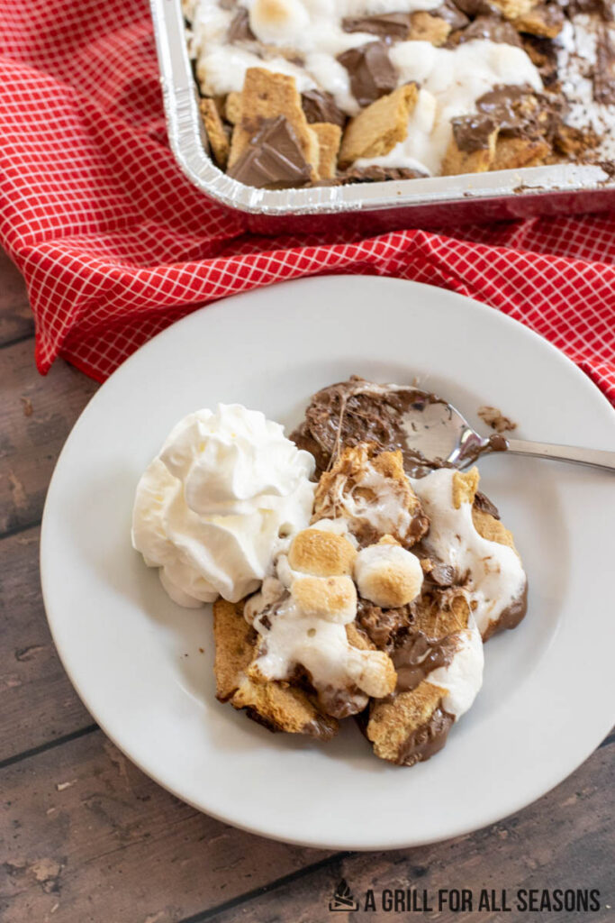 grilled smores casserole recipe served on plate with whipped cream and spoon