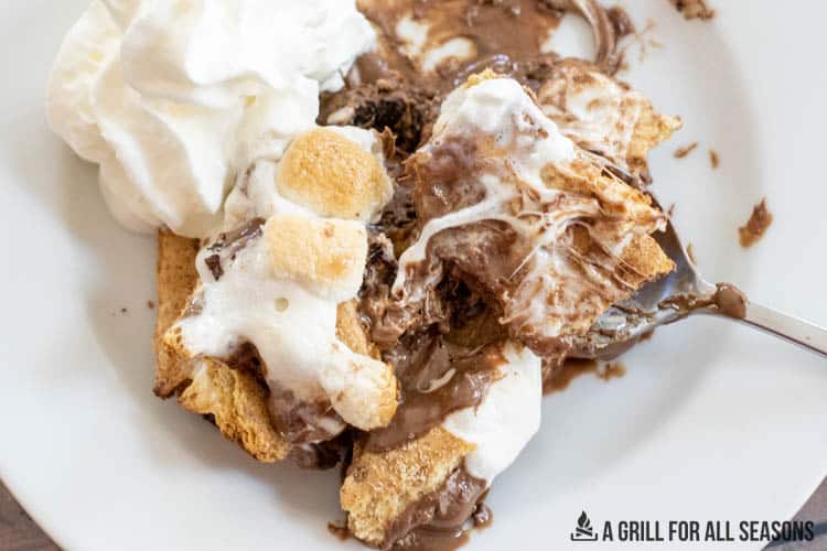 close up of grilled smores casserole recipe served on plate with whipped cream and spoon