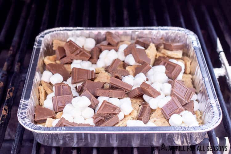 aluminum pan with graham crackers, chocolate, and mini marshmallows on grill