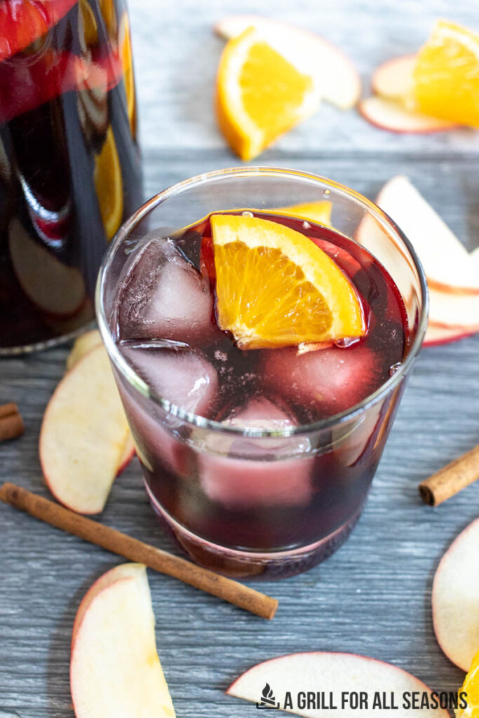 glass of bourbon sangria with pitcher and sliced fruit in background