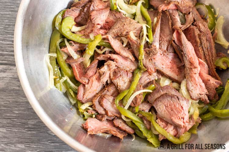 sliced steak with cooked onions and peppers in large bowl