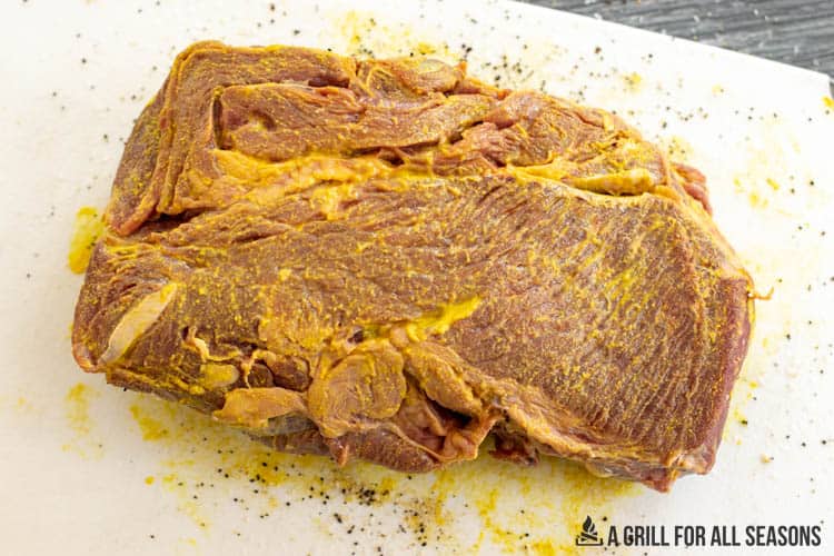 chuck roast covered in yellow mustard on cutting board