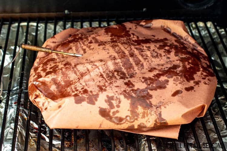 meat wrapped in butcher paper on smoker grates