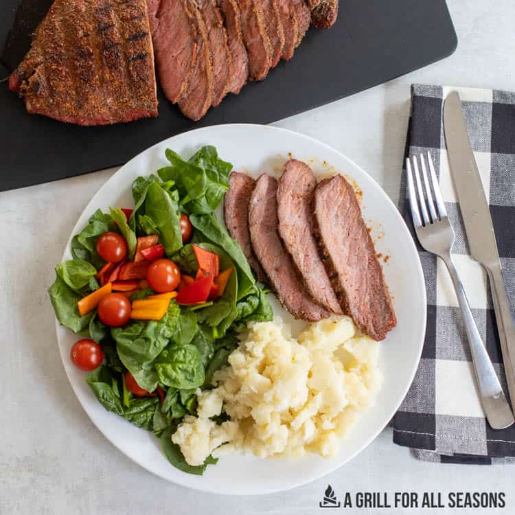 slices of london broil on a plate with mashed potatoes and salad