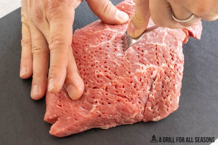 london broil being tenderized with a fork