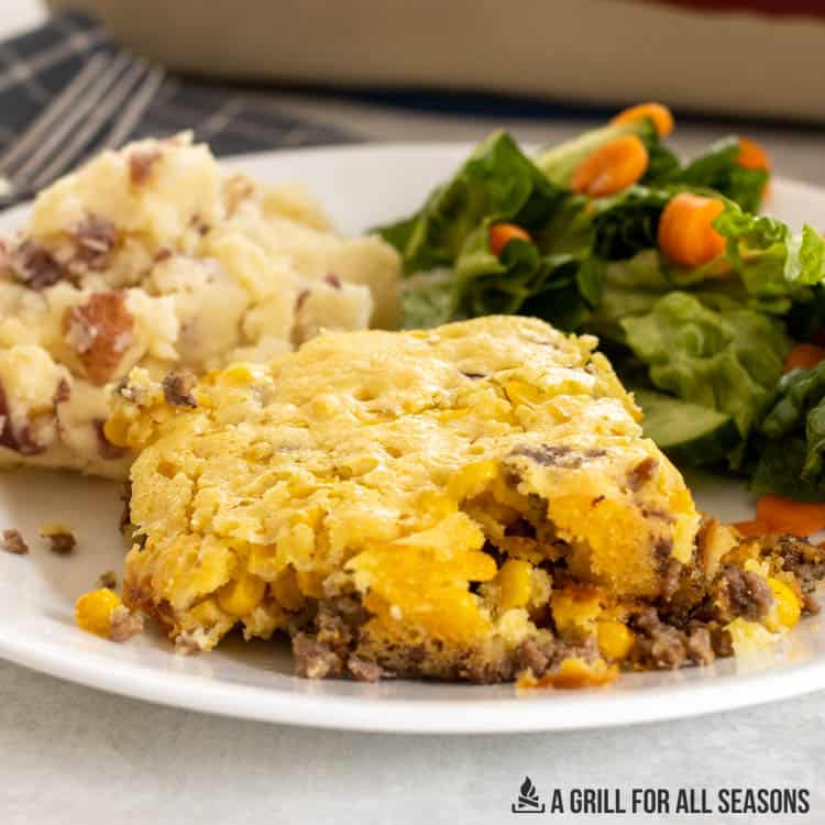 hamburger corn casserole recipe served on plate with salad and mashed potatoes.
