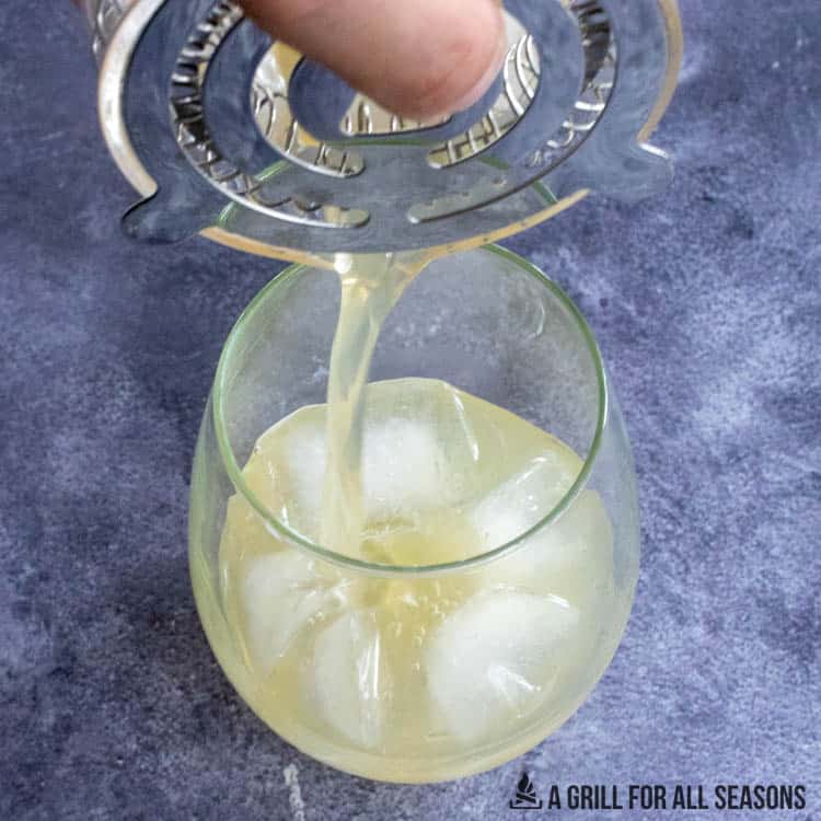 straining cocktail into glass with ice