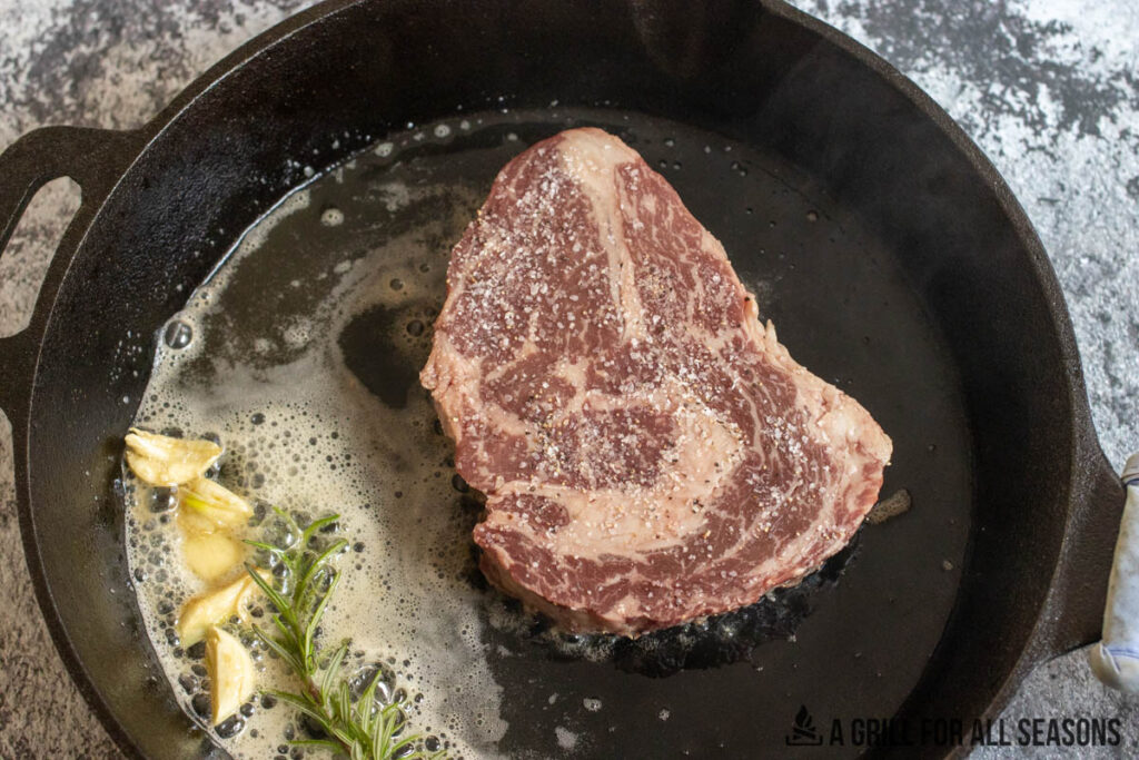 waryu ribeye sitting in skillet with butter, garlic, and herbs