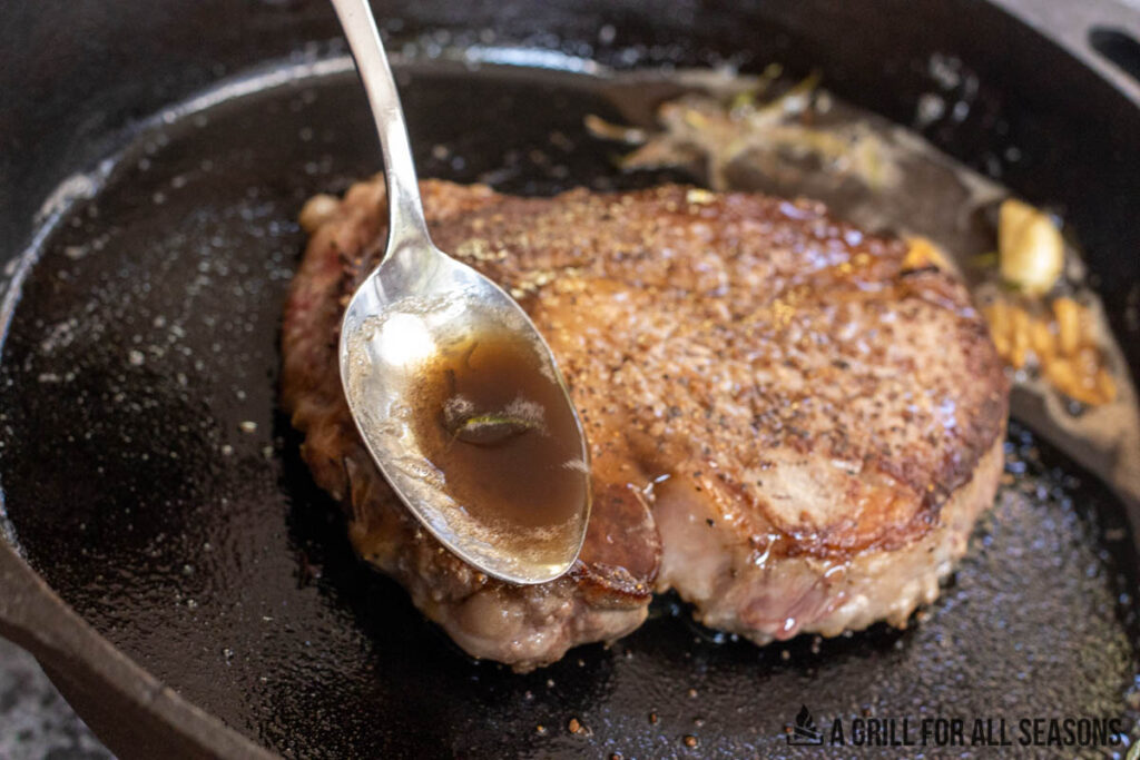 spoon ladeling hot oil over steak