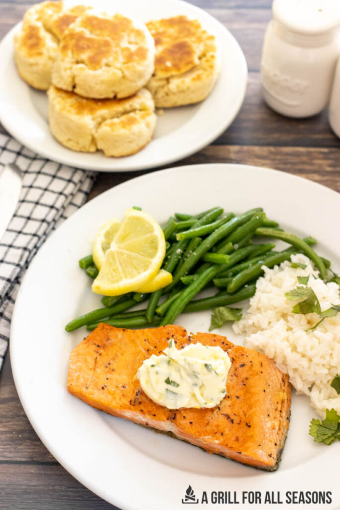 salmon topped with herb butter plated with green beans, rice, and lemon slices