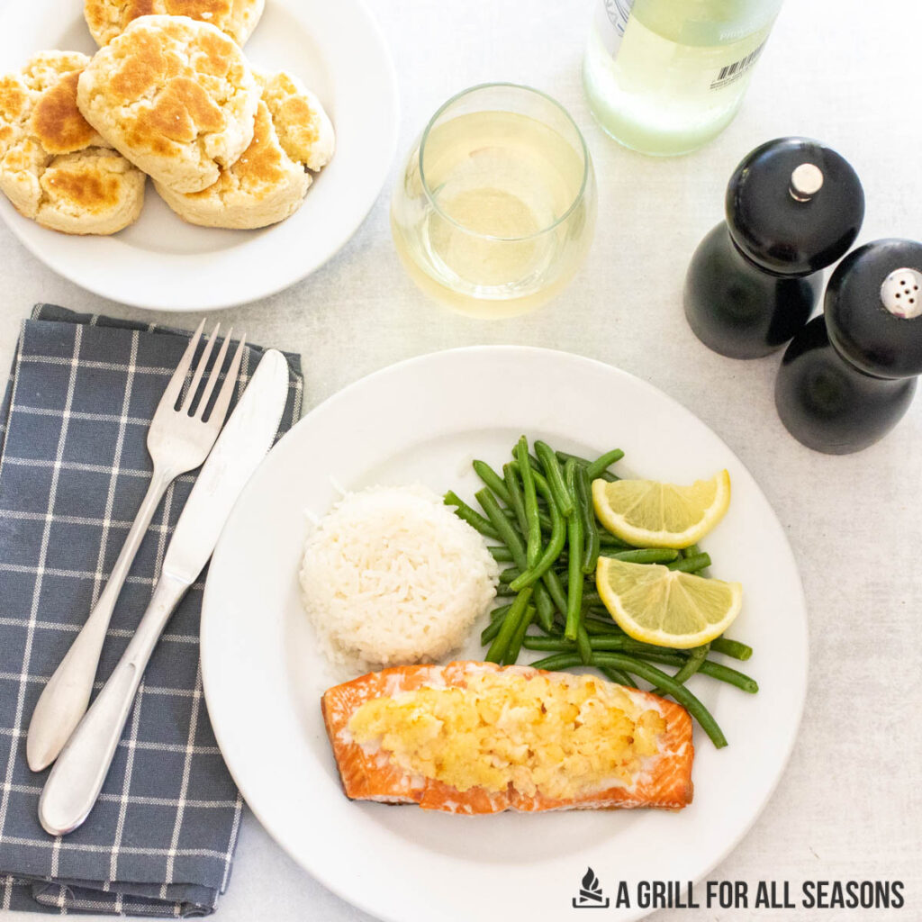 plate of stuffed salmon and sides with salt and pepper shakers, glass of white wine, and plate of biscuits