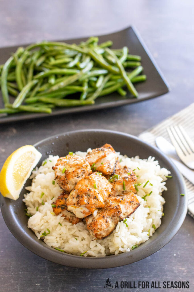grilled cajun salmon bites in bowl with platter of green beans behind
