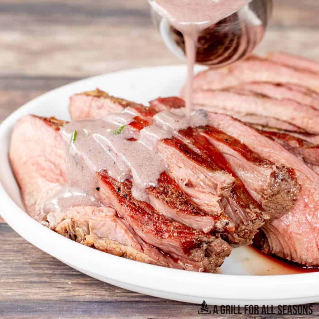 traeger tri tip recipe with peppercorn sauce being drizzled over slices