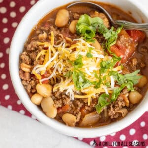 venison chili recipe served in white bowl topped with cheese and cilantro close up