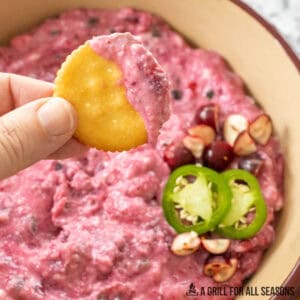 cranberry jalapeno dip recipe on a cracker being held up in front of serving bowl