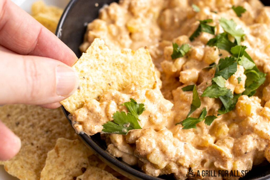 hand dipping a chip in the elote dip