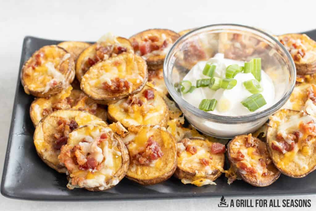 loaded potato bites topped with cheese and bacon with a bowl of sour cream to dip