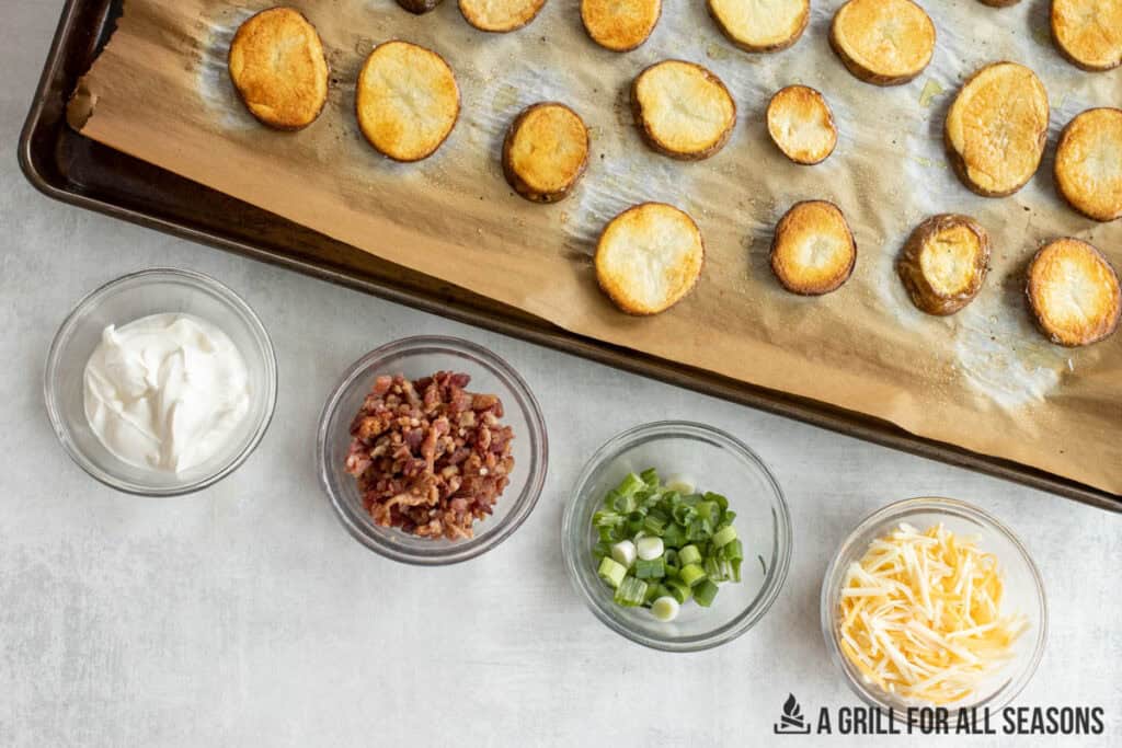 slices of roasted potato on baking tray with small bowls of toppings to be added on the side