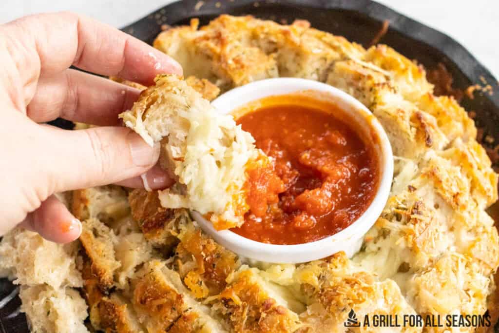 hand dipping a piece of cheese stuffed garlic bread into marinara sauce