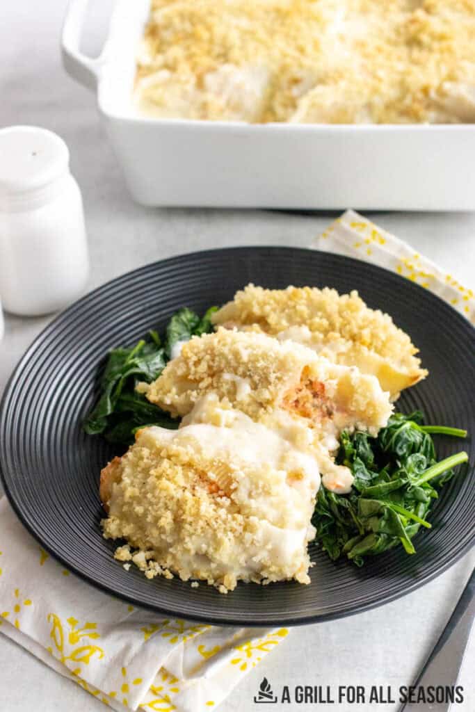 salmon stuffed shells on dinner bed on bed of spinach with casserole dish behine
