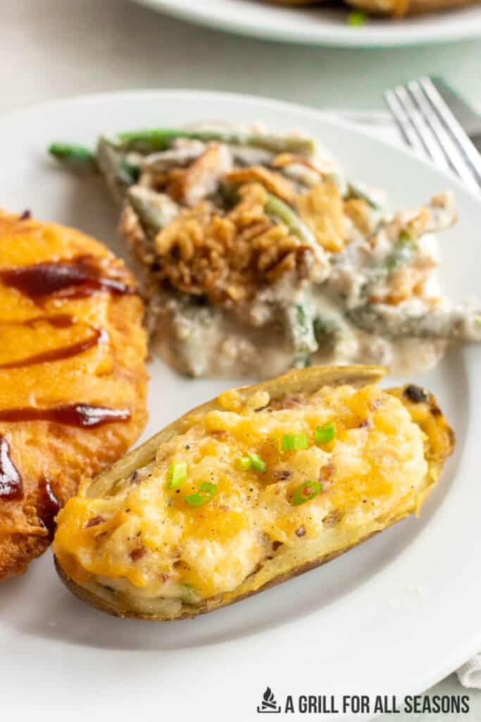 one of the smoked twice baked potato on a plate with chicken and green beans