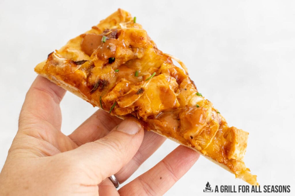 hand holding up a piece of bbq chicken flatbread