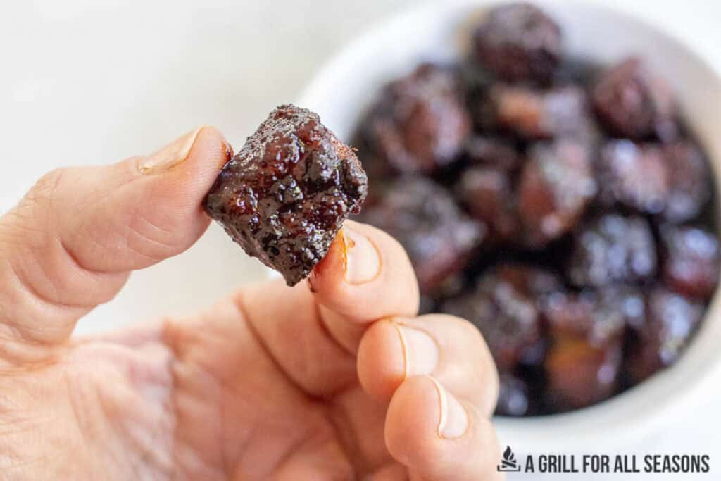 hand holding up a piece of candied pork belly