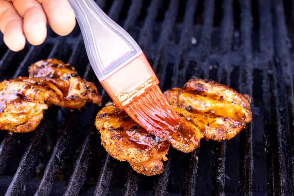 hand brushing hot honey on grilled chicken thighs