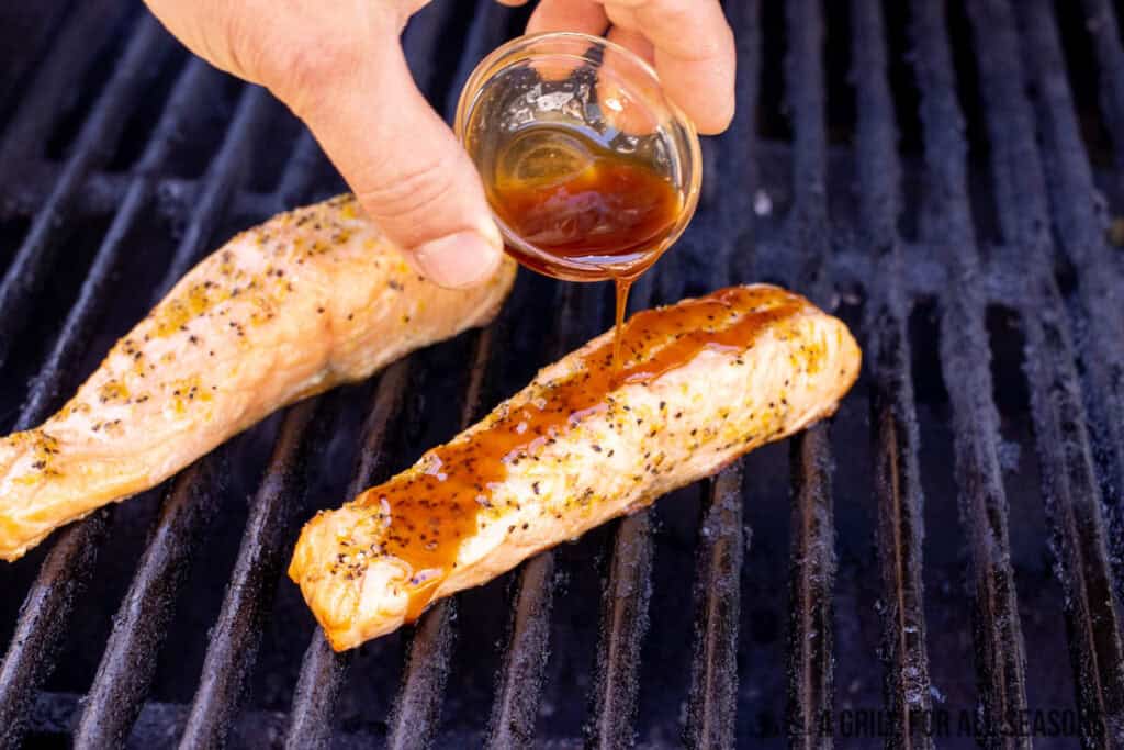hot honey salmon on grill with sauce being poured on