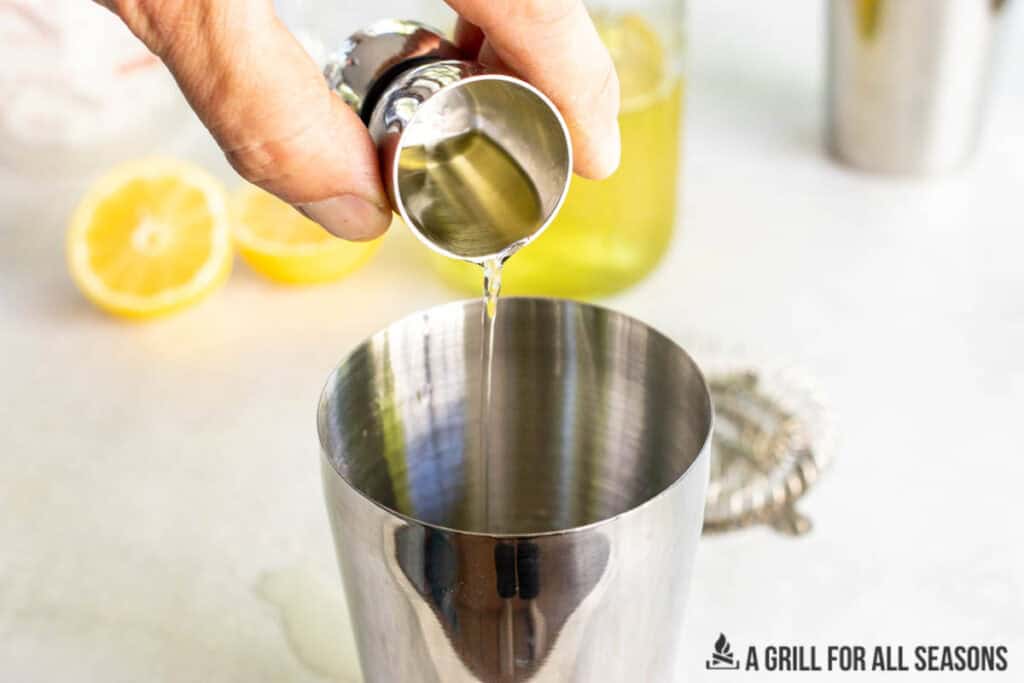 hand pouring limoncello into shaker