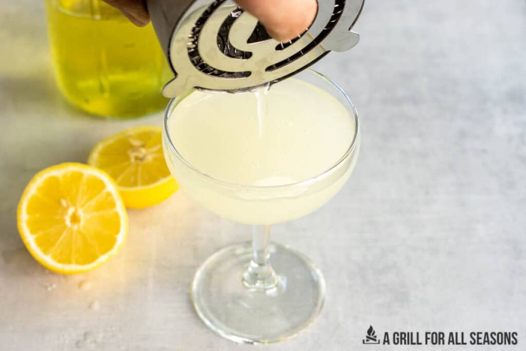 hand pouring drink throw strainer into glass