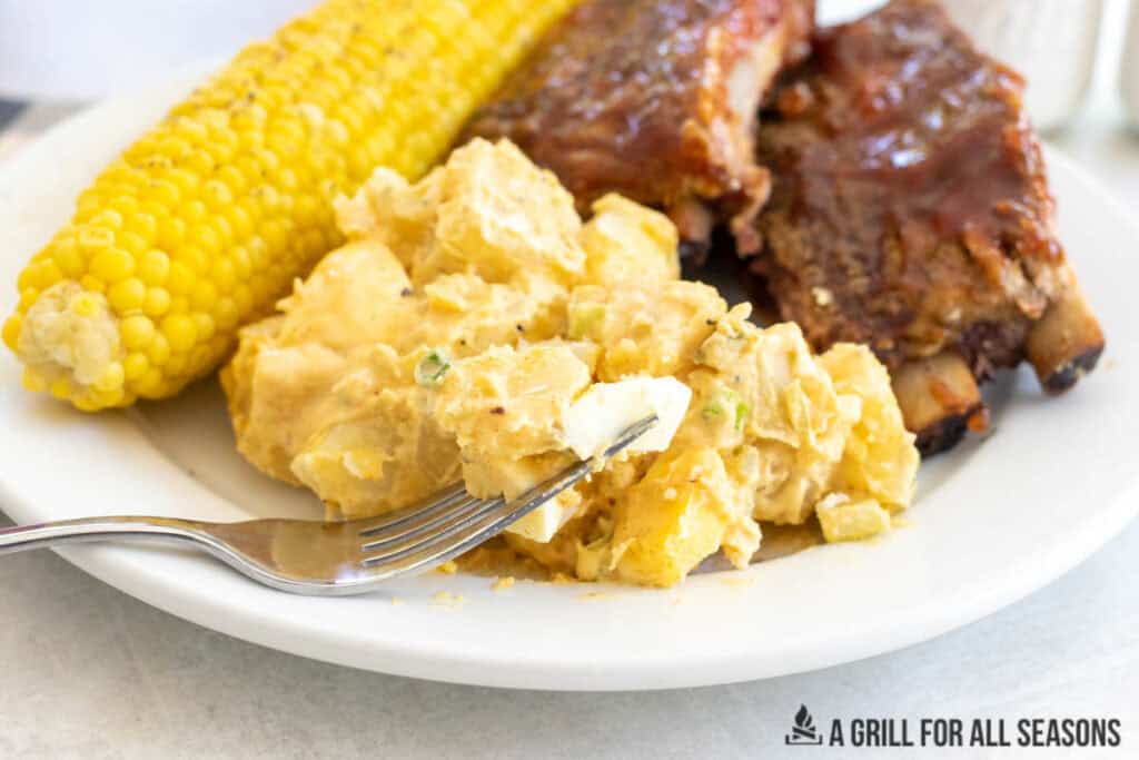 bite of southern potato salad on fork resting on plate with bbq ribs and corn on the cob