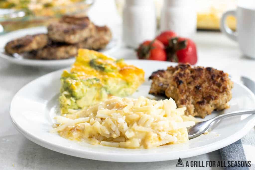 plate with cheesy breakfast potatoes, quiche, and sausages