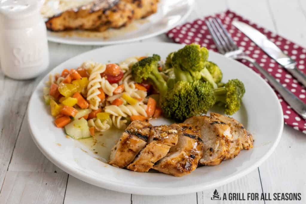 slices of honey mustard grilled chicken breast on dinner plate with pasta salad and broccoli