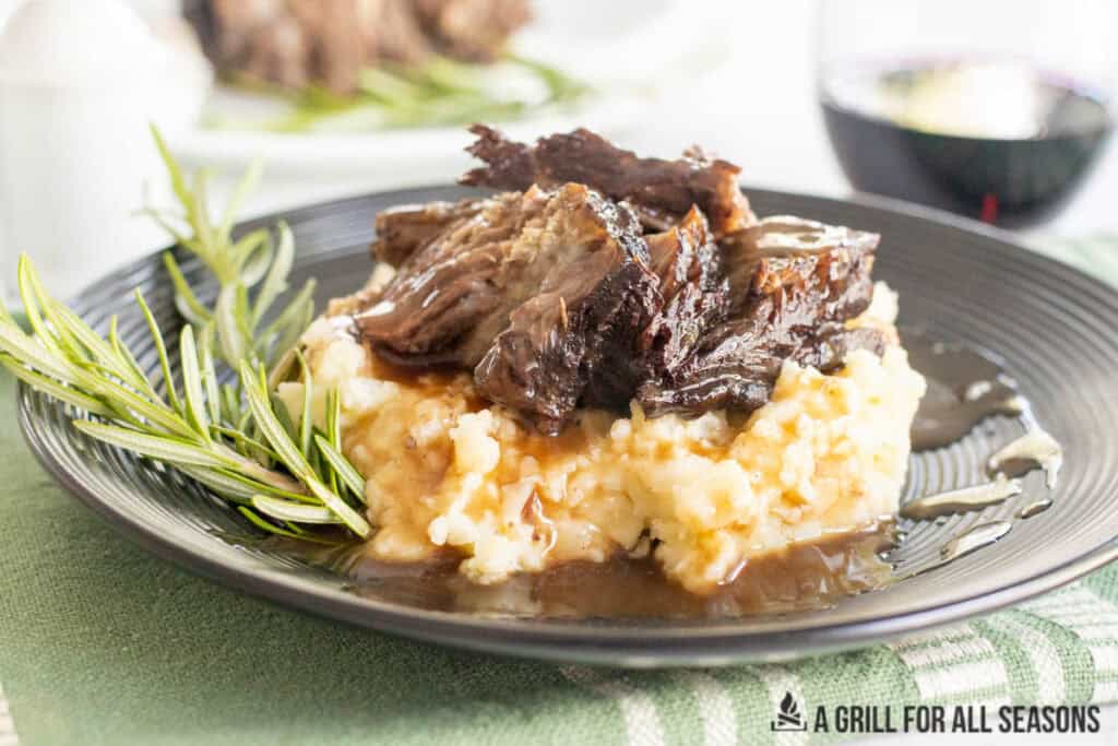 braised chuck roast with gravy served on dinner plate with platter behind