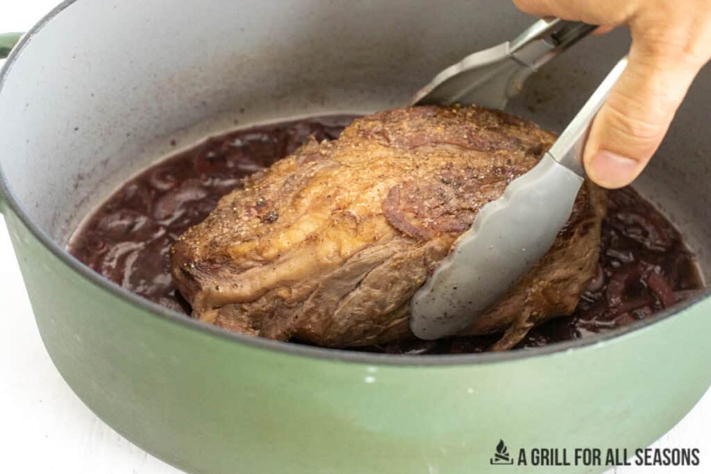 hand using tongs to add beef back to pot