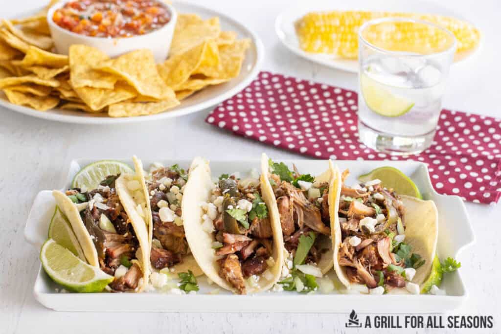 platter of smoked carnitas tacos with smoked salsa and tortilla chips and corn on the cob behind
